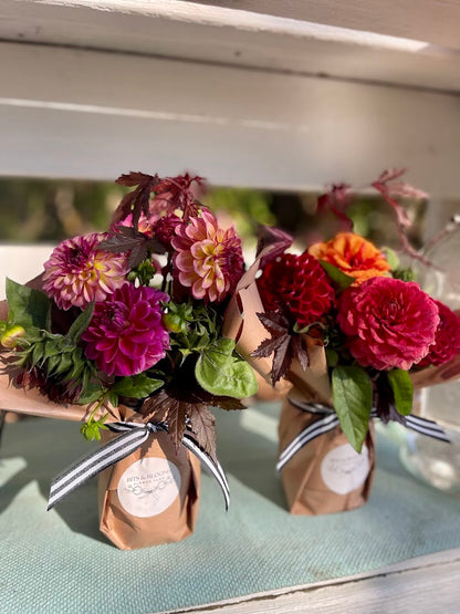 Two small bouquets of flowers in paper bags on a wooden surface.