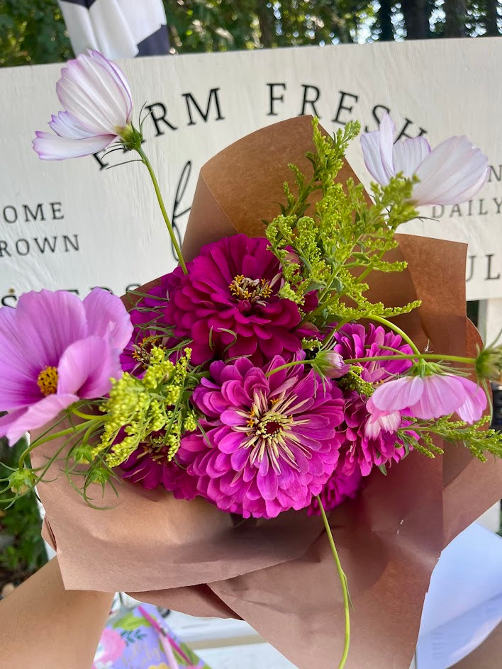 Bouquet of pink and purple flowers in brown paper packaging with a blurred background.